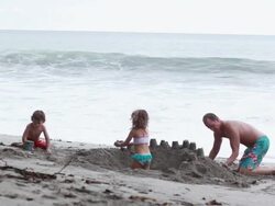 MS Man, boy and girl build sandcastle on beach with wave break / Montezuma, Puntarenas, Costa Rica Stock Footage