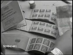 1945: ENGLAND WAR FINANCE: MS British woman & boy purchasing war stamps. CU War stamps being torn, handed for money. INT VS Workers on line at pay booth, getting money. DRAMATIZATION: Two men at booth '... they're taking more income taxes from me...' Instructional Video