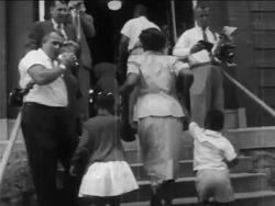 B/W 1950s low angle REAR VIEW Black parents walking their children up stairs into desegregated school Stock Footage