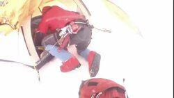 Mountain climbers secure their gear in a tent while snow and wind blow around them. Stock Footage