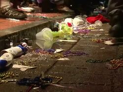 Medium Shot - People walking near trash strewn about edge of sidewalk; mostly cups, bottles, and colored plastic beads / New Orleans Louisiana Stock Footage
