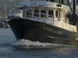Commercial fishing boat heading out to sea from a small New England fishing village - front view as boat comes towards camera - camera tilts down until only bow plowing through the water is seen - 3 Stock Footage