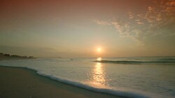 WIDE SHOT sunrise over ocean washing up on beach Stock Footage
