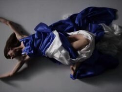 woman with blue silk fabric draped around her laying down before lifting legs up to camera Stock Footage