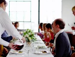 MS R/F waitresses bringing food and wine to table of friends sitting at dinner party Stock Footage