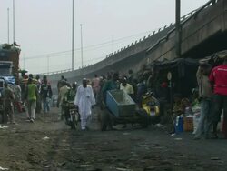 WS View of pedestrians and motorcycles passing in front of collection and weighing building for scrap metal by motorway bridge / Lagos, Nigeria Stock Footage