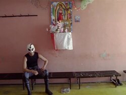 Medium shot portrait of luchador 'Cometa Negro' on bench under altar of Catholic saint / Queretaro, Mexico Stock Footage
