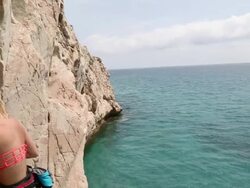 Young woman climbs vertical rock cliff above sea Stock Footage
