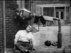 B/W 1917 cop Charlie Chaplin holding bent street lamp over head of large seated man (Eric Campbell) Stock Footage