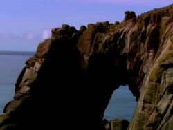 LOW AERIAL, Rock arch and Longships lighthouse, Cornwall, England Stock Footage