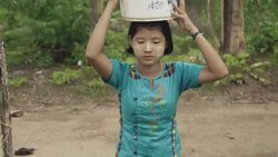 M/S STEADYCAM front, Burmese teenage girl carrying water to her house in a rural area Stock Footage