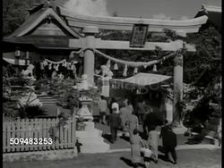 1937: JAPANESE HAWAIIAN RELIGION: WS U.S. & Japanese flag hanging over Japanese entering temple. LA MS Japanese sign. HA WS People entering archway. INT VS Japanese in traditional kimonos kneeling, praying, altar, ritualistic ceremony, bowing. Hawaii Instructional Video
