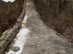 A beautiful section of the Great Wall of China. A snow-covered path leads up to a tower that rests on jagged rocks and mountains.  Stock Footage