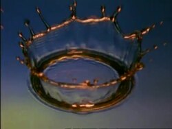 High Speed CU golden coloured water drop splashing into blue water, high angle Stock Footage