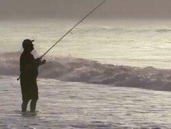 A man fishes in the ocean early morning.  The tide breaks around his legs.  Stock Footage