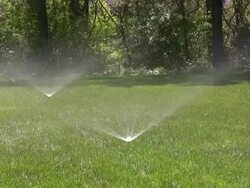 Sprinklers. Agricultural Sprinkler spraying water on back yard green grass. Stock Footage