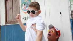 Son sitting on fathers lap and father points up to the sky then lift son up and down as son smiles and they are both wearing sunglasses Stock Footage