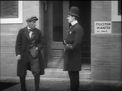 B/W 1917 policeman Charlie Chaplin hitting man laughing at him with nightstick outside of station Stock Footage