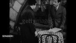 1936: FRANCE: DRAMATIZATION: Gendarmes talking outside Cafe du Sport. INT Middle-aged woman entering cafe SOT woman sitting at table w/ 'Mr. Gabriel' who promises to help her son, husband for 20,000 francs. MS Elder fisherman staring. WS EXT Cafe. Instructional Video