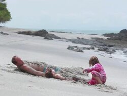 MS Man and boy lie on sand covered in sand while man and girl cover boy with sand then boy sits up on beach / Montezuma, Puntarenas, Costa Rica Stock Footage