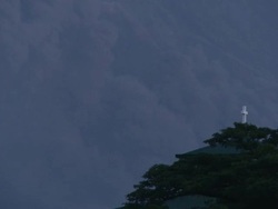 Ash cloud from pyroclastic flow on Mayon volcano drifts behind trees and church at dawn, Philippines, December 2009 Stock Footage