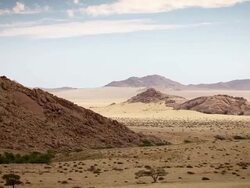 WS AERIAL T/L View of Desert crags interrupt flat scrubby grasslands and sand and huge golden distance under soft blue sky and streaming white clouds / Windhoek, Namibia Stock Footage