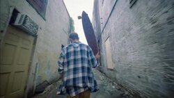 Skater walks down urban alleyway carrying custom longboard overhead Stock Footage