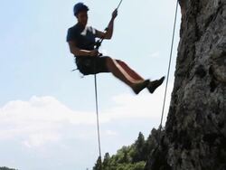 PAN downwards with climber rappelling (abseiling) from cliff Stock Footage