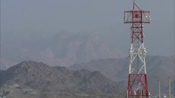 A flag waves in the wind on a radio tower near a mountain. Stock Footage