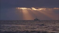 Sunbeams filter through purple clouds onto a fishing boat below. Stock Footage