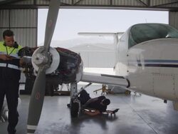 TS WS aircraft mechanics working on engines and landing gear of twin engine propeller aircraft in hangar, RED R3D 4K Stock Footage