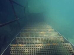 Diver swimmin along metal steps underwater Stock Footage