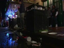 Medium Shot Low Angle - People walking on street at night; garbage can overflowing, trash on street / New Orleans Louisiana Stock Footage