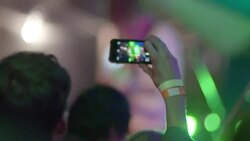 Young man snaps photo with smartphone at outdoor rock concert Stock Footage