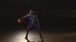 A male basketball player dribbles a ball between his legs and then holds the ball while looking very intense. Stock Footage