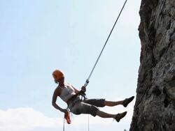PAN downwards with climber rappelling (abseiling) from cliff Stock Footage