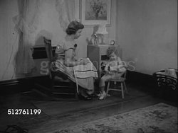 1953: TWO YEAR OLD: Girl sitting on chair next to mother's, putting on her shoe, mother handing her dress, child preparing to put on clothes by herself. Instructional Video