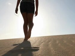 Teenage girl walks into sand dunes, riases arms to sun Stock Footage