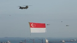 W/S PANNING SHOT OF HELICOPTOR CARRYING GIANT SINGAPORE FLAG,CARGO SHIPS IN B/G ,NATIONAL DAY Stock Footage