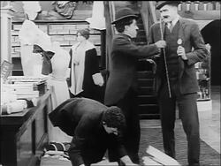 B/W 1916 Man (Albert Austin) giving stacks of thin boxes to Charlie Chaplin / Chaplin dropping boxes Stock Footage