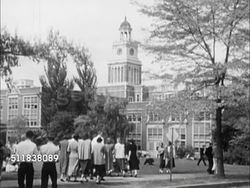 1950: DENVER, COLORADO: EAST SIDE DENVER HIGH SCHOOL: WS Students walking on sidewalk w/ school building w/ clock tower BG. Groups of students sitting on lawn. Group of male students sitting together. Instructional Video