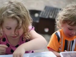 MS Little girl beading while little boy eating dry cereal in front of barbecue pit at picnic table / Toronto, Ontario, Canada Stock Footage