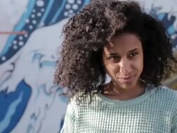 Young woman with curly hair looking into camera, smiling, laughing in sunshine Stock Footage