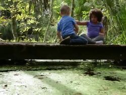WS Boy and girl playing with toy dinosaurs on wooden bridge in woodland. Stock Footage