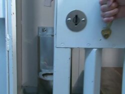 Medium pan-left zoom-in - Hands close the door to a detention cell and turn the lock with a key. / USA Stock Footage