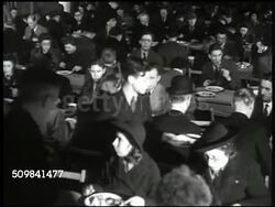1945: BRITISH RESTAURANT: EXT WS Women entering 'British Restaurant.' HA INT WS Men & women eating at long tables. MS Men on line being served food at counter. MS Woman moving cut potatoes from pan. MS People eating food at long tables. Instructional Video