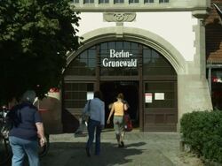 Exterior shot. Sunny day with people walking into the Bahnhof Grunewald station in Berlin Stock Footage
