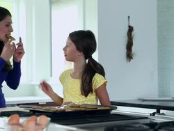 MS DS daughter feeding mom a cookie while standing at counter in kitchen of contemporary home Stock Footage