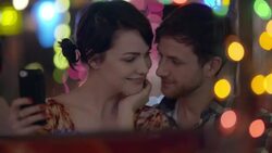 Young woman takes a selfie with smartphone as boyfriend kisses her cheek Stock Footage