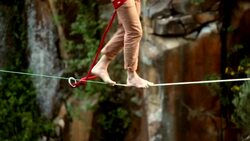 Man traverses highline stretched above waterfall, valley Stock Footage